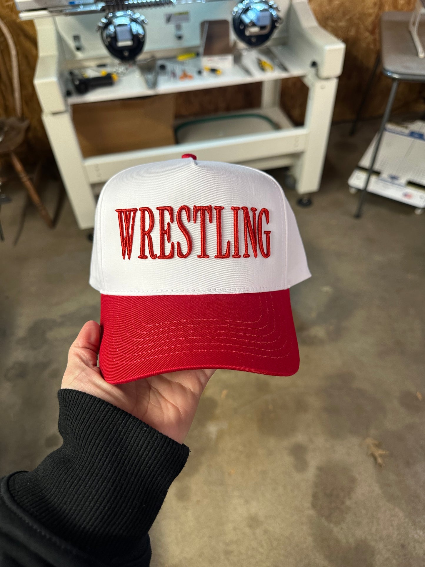 Red and white cap with 'Wrestling' text held by a person in an indoor setting.