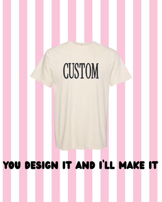 An off-white short-sleeve t-shirt with the word 'CUSTOM' printed in black serif letters on the chest, set against a pink and white striped background with the text 'YOU DESIGN IT AND I'LL MAKE IT' below.