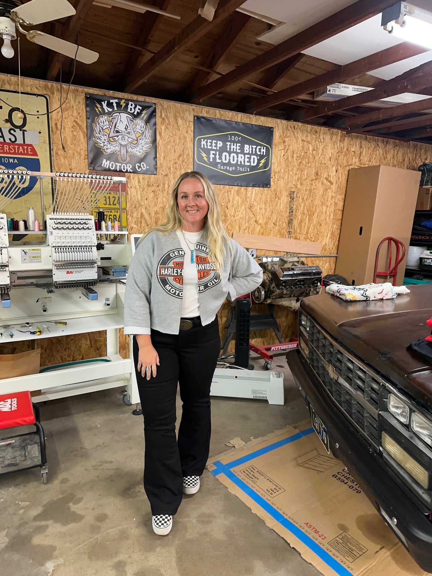 Person standing in a workshop with tools and equipment around and embroidery machine and squarebody
